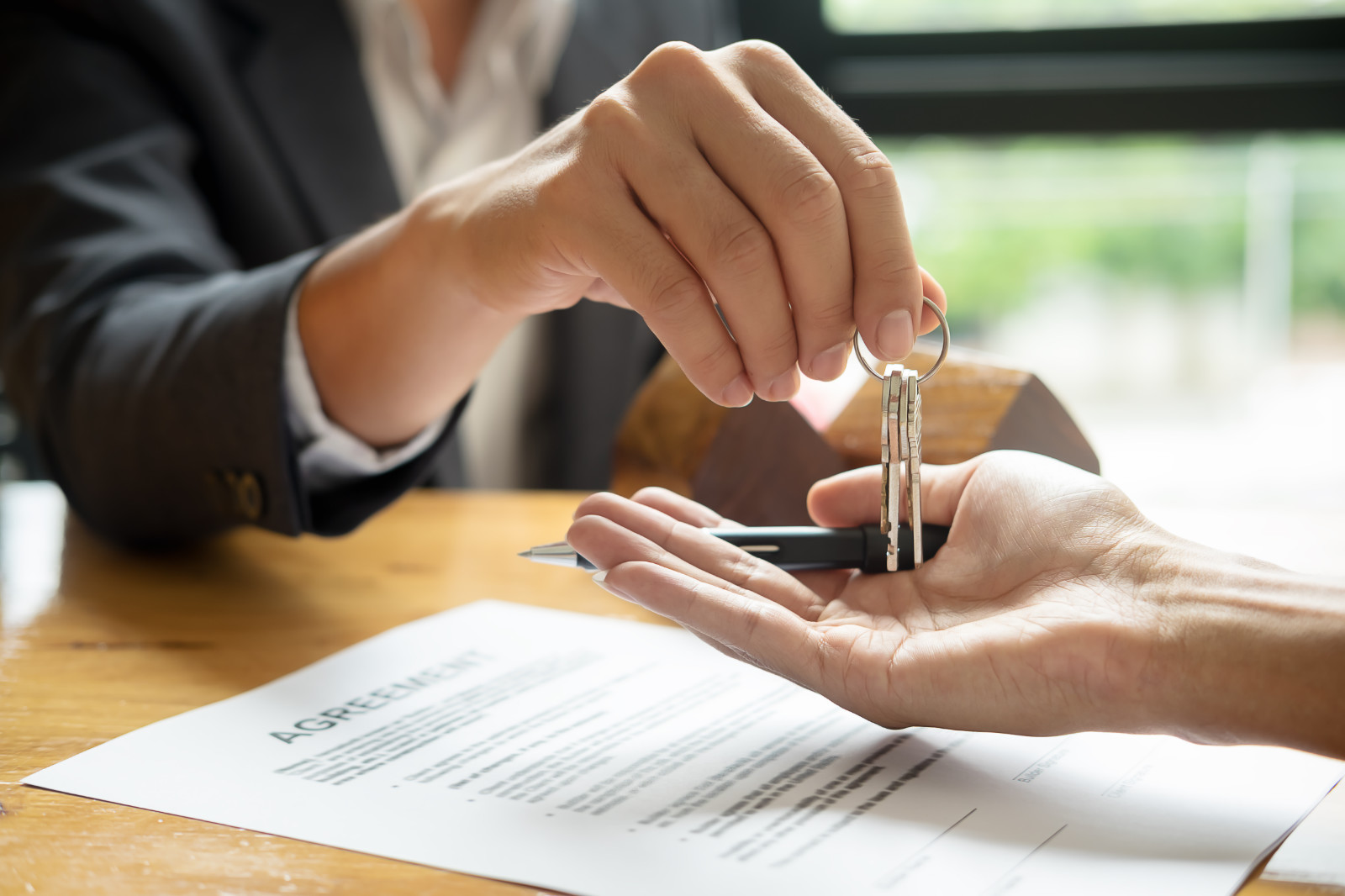 real estate agent holding house key to his client after signing contract agreement in office,concept for real estate, moving home or renting property